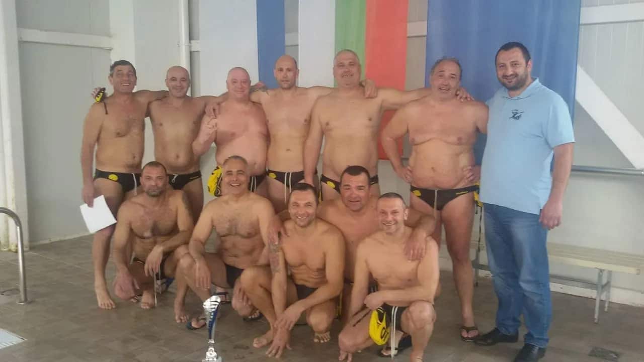 The team with a cup at an indoor pool, under flags