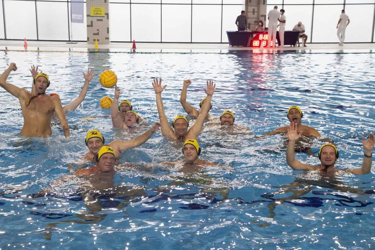 Players in yellow caps celebrating in the water of an indoor pool