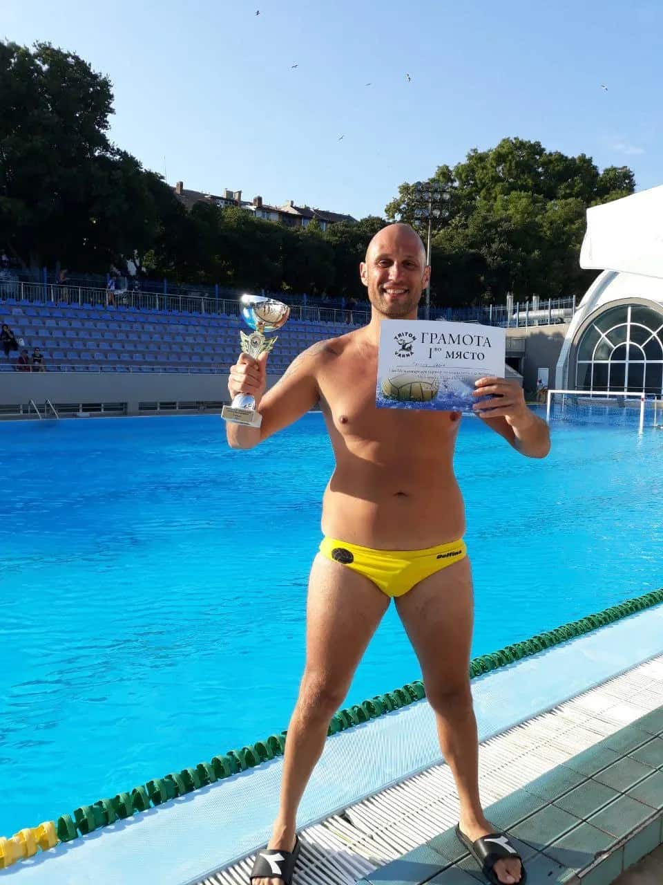 A player with a cup and the certificate by the outdoor pool